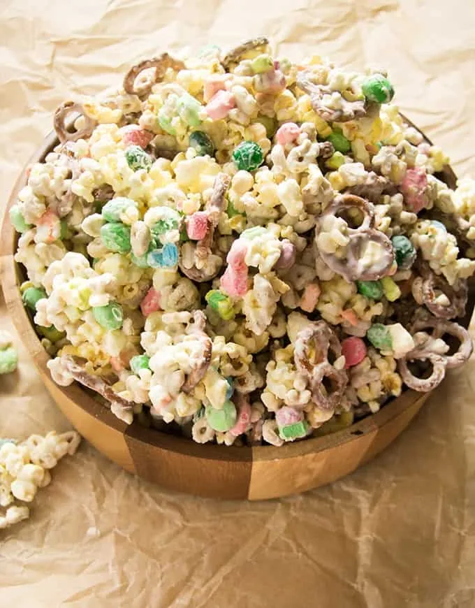 A wooden bowl filled with St. Patrick's Day snack mix, featuring popcorn, colorful marshmallows, chocolate-covered pretzels, and festive candies, perfect for holiday celebrations.