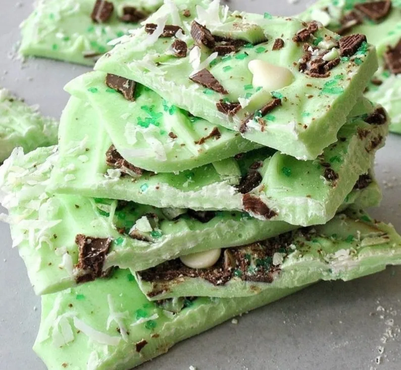 Pieces of mint chocolate bark with a green base, topped with white chocolate chips, chocolate chunks, shredded coconut, and green sprinkles, perfect for St. Patrick's Day desserts or Irish-inspired treats.