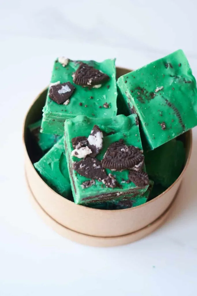 Vibrant green mint chocolate fudge pieces topped with crushed Oreos, arranged in a round container, perfect for St. Patrick's Day desserts or festive Irish-inspired treats.