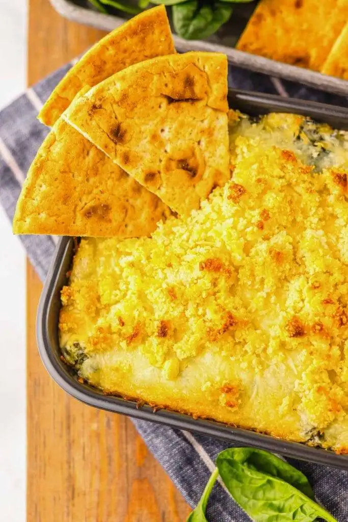 Creamy spinach and cheese dip topped with golden breadcrumbs, served with pita chips—an irresistible addition to your Irish party food spread.