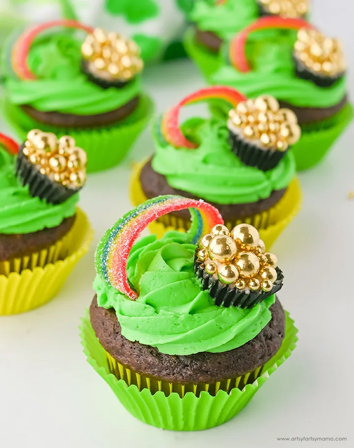 Chocolate cupcakes with vibrant green frosting, topped with rainbow candy and gold candy coins to resemble a pot of gold, perfect for St. Patrick's Day desserts or festive Irish celebrations.