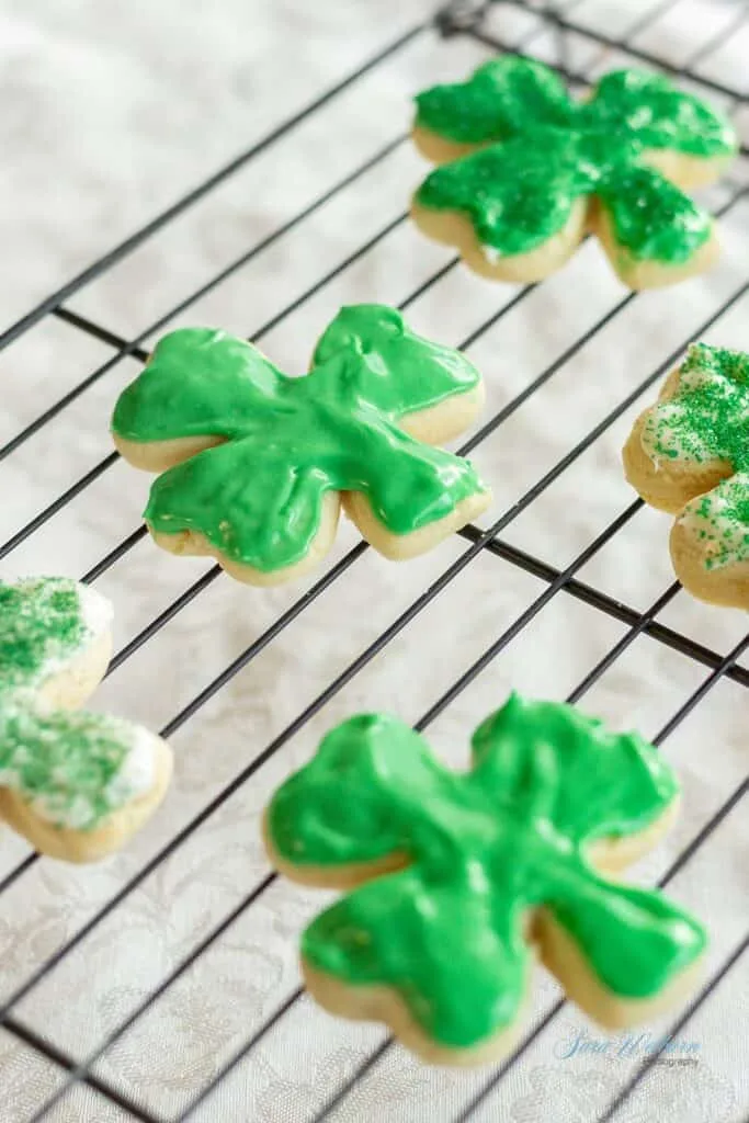 Shamrock-shaped sugar cookies with green icing and sprinkles cooling on a wire rack, perfect for St. Patrick's Day desserts or festive Irish treats.