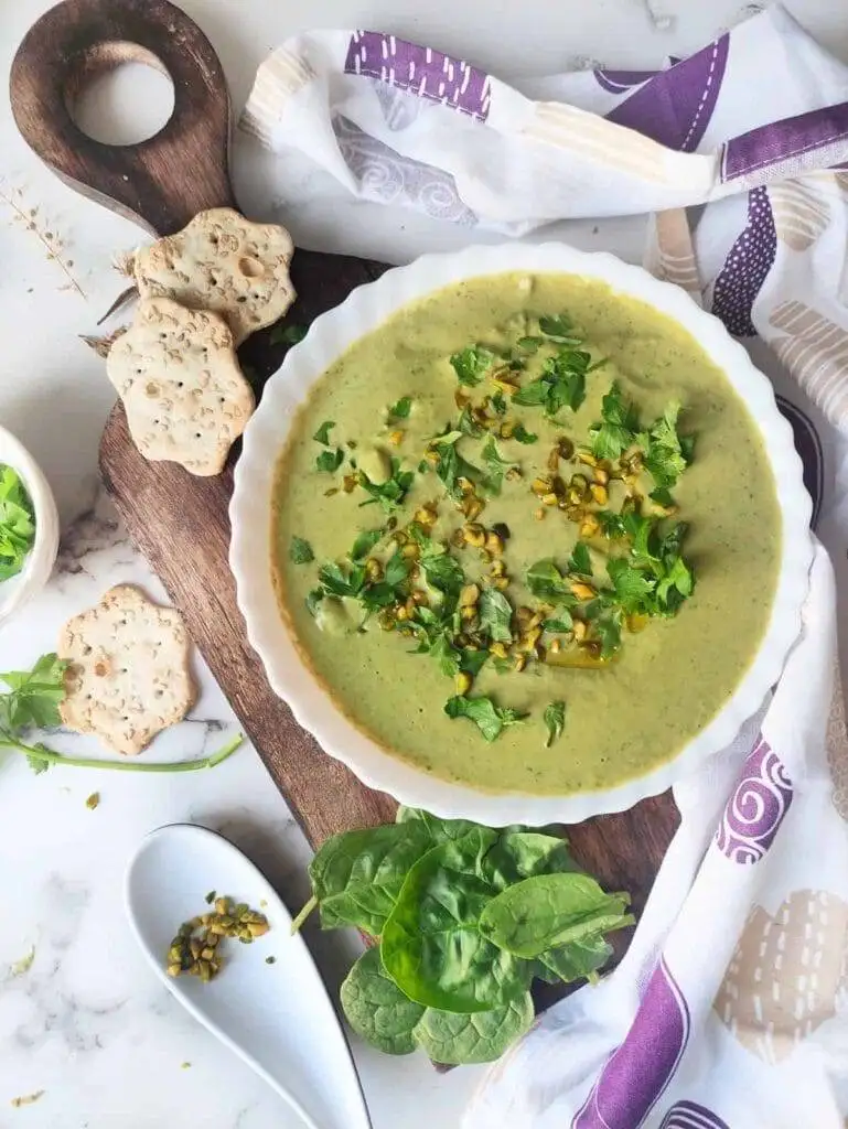 A vibrant bowl of creamy spinach and pistachio dip garnished with fresh parsley and chopped pistachios, served with seed crackers—an elegant Irish party food option.