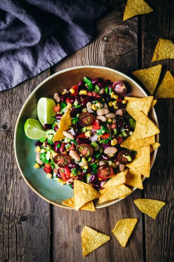 A colorful bowl of fresh Texas caviar made with beans, corn, tomatoes, and herbs, served with lime wedges and tortilla chips—perfect for a vibrant Irish party food spread.