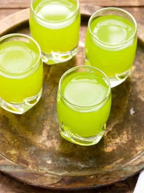 Four vibrant green shots served in small glasses, arranged on a rustic golden tray, creating a bright and festive presentation.