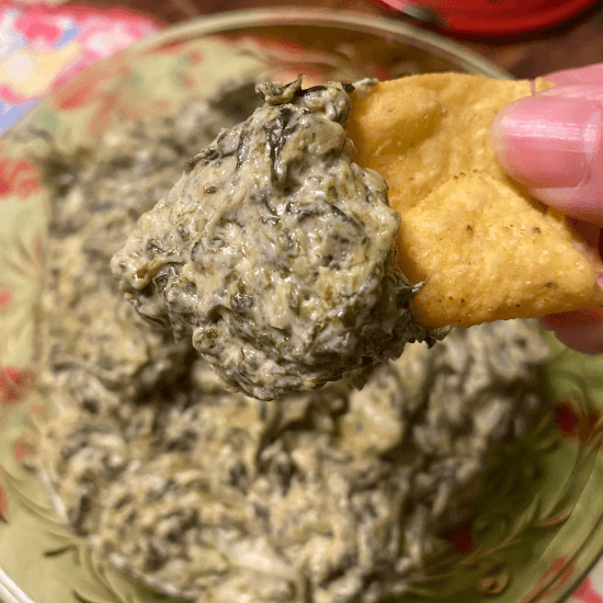 A creamy, farm-to-table spinach dip scooped onto a crispy cracker, highlighting the richness of fresh, locally sourced ingredients. The dip’s velvety texture and deep green color showcase farm-fresh spinach blended with savory, budget-friendly flavors, making it a perfect appetizer for any occasion.