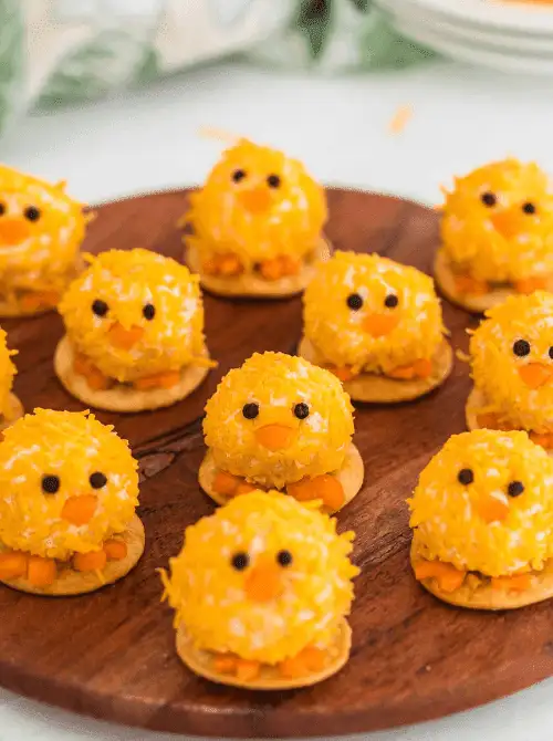 Adorable baby chick mini cheese balls coated in shredded cheese, served on crackers—perfect for easy Easter finger food ideas. A fun and festive appetizer for spring gatherings.