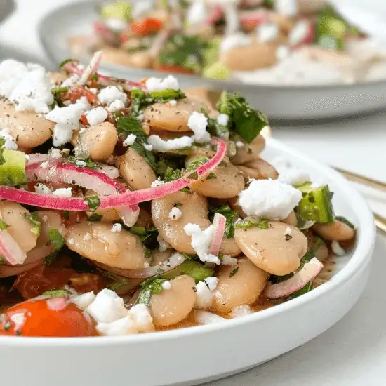 A fresh and flavorful farm to table bean salad, featuring tender butter beans, pickled red onions, cherry tomatoes, crumbled feta, and vibrant herbs. The dish is lightly dressed, allowing the natural flavors of the locally sourced ingredients to shine. Served on a simple white plate, this wholesome meal captures the essence of farm to table eating—fresh, nourishing, and packed with flavor.