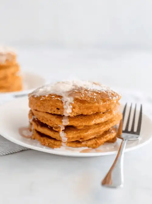 Stack of fluffy carrot cake pancakes drizzled with a sweet glaze, served on a white plate with a fork, perfect for a budget-friendly Easter brunch.