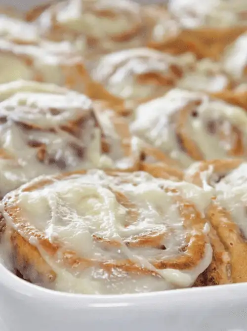 Close-up of freshly baked cinnamon rolls in a baking dish, generously topped with creamy icing—an irresistible treat for a budget-friendly Easter brunch.