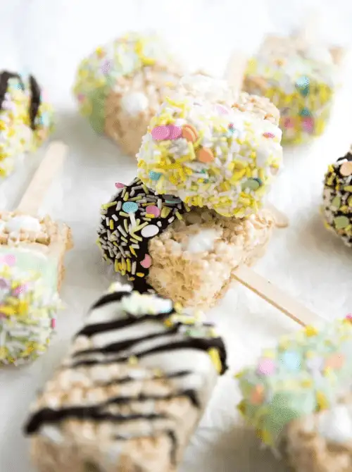 Festive Easter Rice Krispie treat pops dipped in chocolate and covered with colorful sprinkles—perfect for easy Easter finger food ideas and a fun holiday dessert!