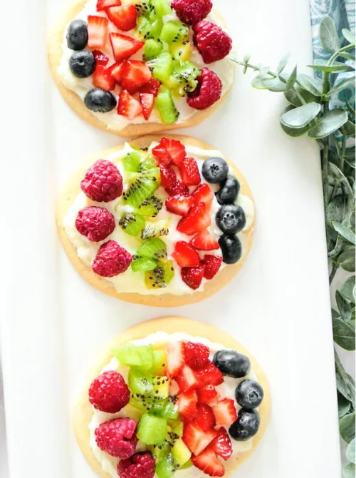 Colorful Easter egg-shaped fruit pizzas made with a sugar cookie base, creamy topping, and fresh berries—perfect for easy Easter finger food ideas and festive spring desserts!

