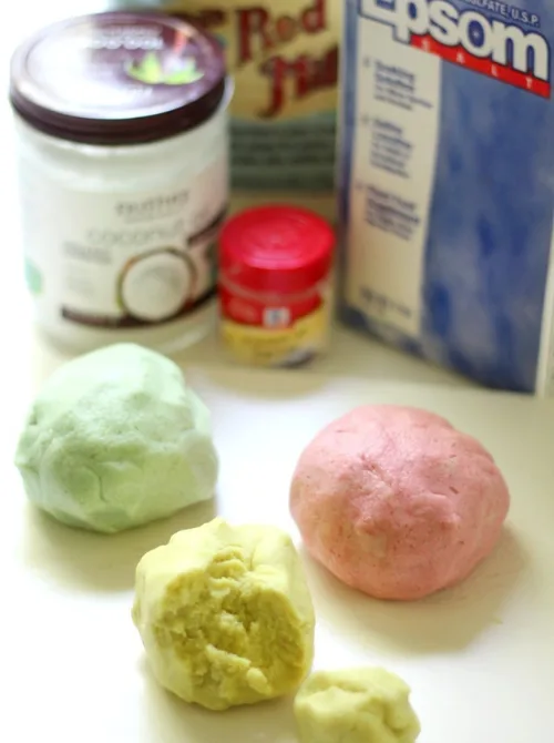 Homemade pastel-colored playdough in soft green, pink, and yellow hues, made from natural ingredients like coconut oil, Epsom salt, and flour, displayed alongside the essential supplies. This fun and sensory-friendly DIY craft makes a fantastic addition to DIY Easter basket ideas, offering a creative, homemade gift that kids will love to play with.