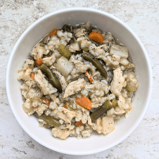 A comforting bowl of farm to table chicken and barley stew, filled with tender shredded chicken, hearty barley, green beans, carrots, and potatoes. The warm, homemade flavors highlight the freshness of locally sourced ingredients, making this nourishing dish perfect for a cozy, wholesome meal.