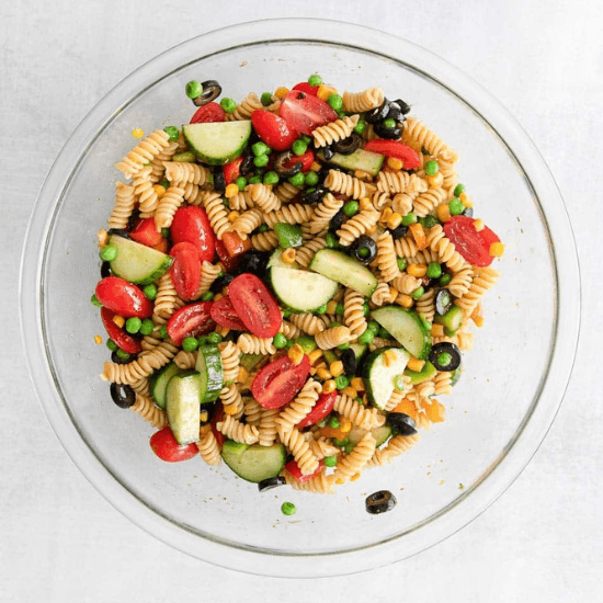 A colorful farm to table pasta salad featuring rotini pasta, crisp cucumbers, juicy cherry tomatoes, black olives, sweet peas, and bell peppers, all tossed in a light dressing. The fresh, locally sourced ingredients bring out vibrant flavors and textures, making this dish a perfect combination of wholesome and delicious.