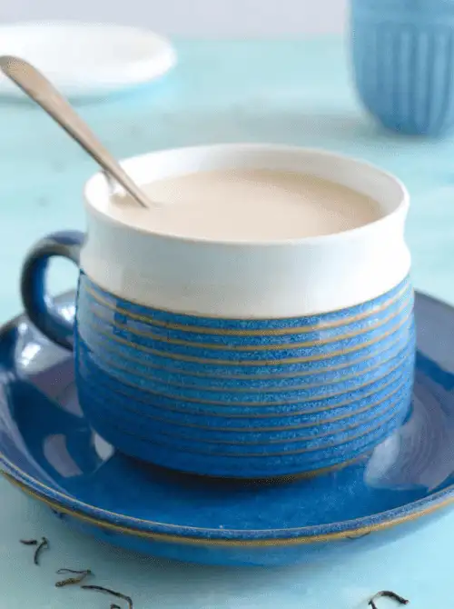 A modern blue and white striped teacup filled with creamy tea sits on a matching saucer with a spoon resting inside—an inviting and stylish addition to your cozy and creative Mother's Day tea party ideas.