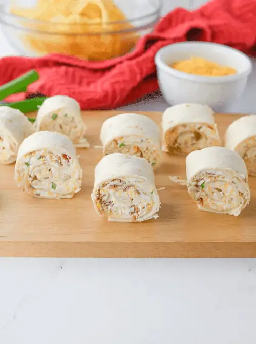 Creamy tortilla pinwheels filled with cheese, green onions, and bits of bacon are neatly arranged on a wooden board—an easy and savory finger food perfect for your Mother’s Day tea party ideas.