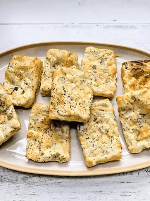 Golden, flaky herb cheese biscuits are arranged on a neutral platter, showcasing their rustic charm and savory aroma—an inviting and flavorful treat to include in your Mother’s Day tea party ideas.