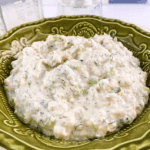 Creamy shrimp salad sandwich spread in a decorative green bowl, featuring a textured mixture with visible herbs and diced celery, ready to serve as a dip or sandwich filling.