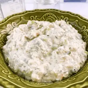 Creamy shrimp salad sandwich spread in a decorative green bowl, featuring a textured mixture with visible herbs and diced celery, ready to serve as a dip or sandwich filling.