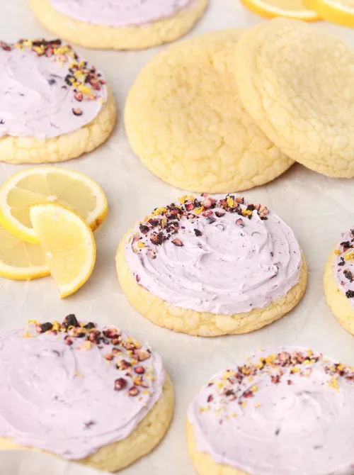 Soft lemon sugar cookies topped with lavender-hued frosting and sprinkled with dried flower petals, styled with fresh lemon slices—an elegant and sweet addition to your Mother's Day tea party ideas.