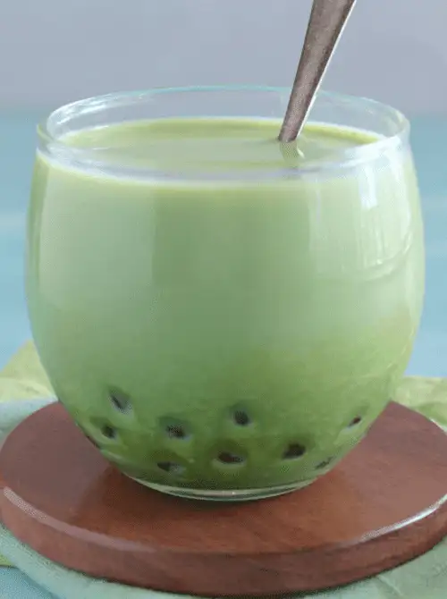 A round glass filled with a creamy green matcha bubble tea, complete with tapioca pearls at the bottom and a spoon resting inside—an eye-catching and fun beverage idea to add a playful twist to your Mother's Day tea party ideas.