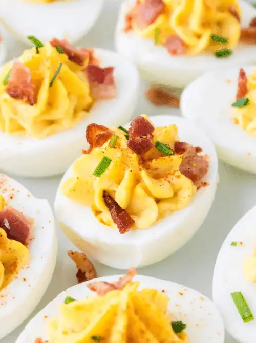 Classic deviled eggs topped with crispy bacon, chopped chives, and a sprinkle of paprika are neatly arranged on a serving tray—bringing a savory, protein-packed bite with a gourmet twist to your Mother's Day tea party ideas.