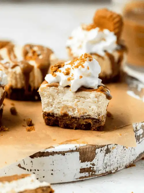 Mini Biscoff cheesecakes topped with whipped cream and cookie crumbles, served on a rustic white tray—an indulgent and delightful dessert option for Mother’s Day tea party ideas.