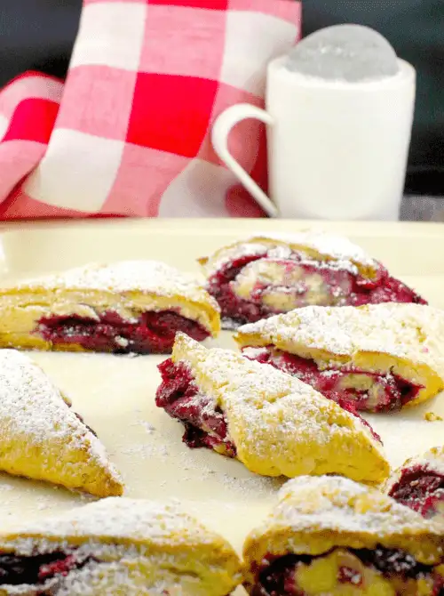 Golden crescent-shaped pastries filled with raspberry jam and dusted with powdered sugar, served with a frothy latte—cozy, fruit-filled treats that add a touch of charm to Mother’s Day tea party ideas.