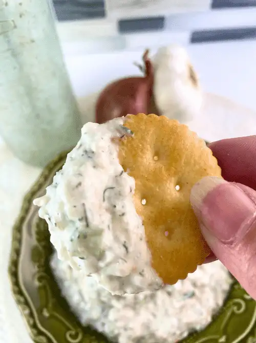 Close-up of a buttery cracker dipped in creamy Shrimp Salad Sandwich Spread, perfect for serving at a Mother's Day Tea party as a savory bite.