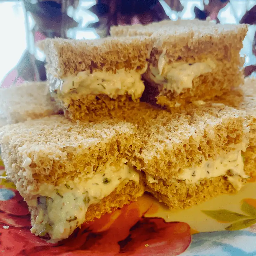 Stacked shrimp salad tea sandwiches made with whole wheat bread, cut into neat squares and arranged on a floral plate, perfect for brunch or party appetizers.
