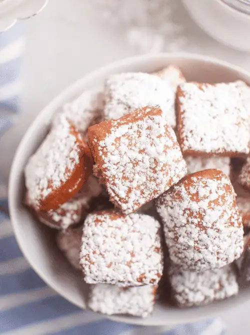 A bowl of fluffy beignets generously dusted with powdered sugar, offering a soft and sweet indulgence—perfect for adding a touch of Southern charm to your Mother's Day tea party ideas.