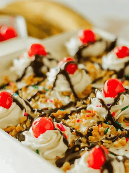 No-bake banana split cake topped with whipped cream, chocolate drizzle, chopped nuts, rainbow sprinkles, and maraschino cherries—an easy 4th of July dessert that’s festive, fun, and crowd-pleasing.