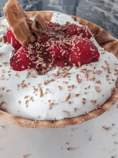 No-bake cherry cheesecake served in a waffle bowl, topped with cherry pie filling, chocolate shavings, and a waffle cone piece—an easy 4th of July dessert that’s fun, festive, and perfect for kids and parties.
