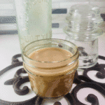 Small mason jar filled with homemade Honey Almond Fluff Creamer, set on a decorative trivet with vintage glass bottles in the background.