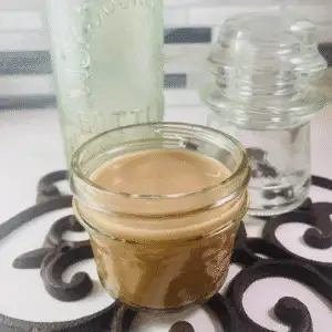 Small mason jar filled with homemade Honey Almond Fluff Creamer, set on a decorative trivet with vintage glass bottles in the background.