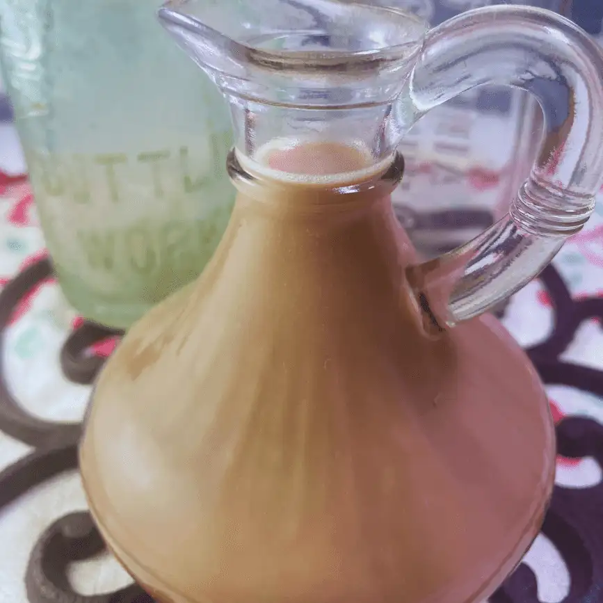 Glass pitcher filled with creamy Honey Almond Fluff Creamer, set on a vintage-style table with a soft, cozy kitchen backdrop—perfect for DIY coffee moments.