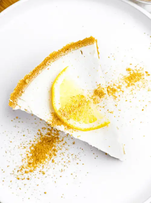 A slice of no-bake lemon pie on a white plate, topped with a fresh lemon wedge and graham cracker crumbs—an easy 4th of July dessert that’s light, creamy, and refreshing.