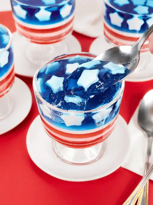 Layered red, white, and blue star-spangled gelatin cups served on white saucers—an eye-catching no-bake treat perfect for easy 4th of July desserts.