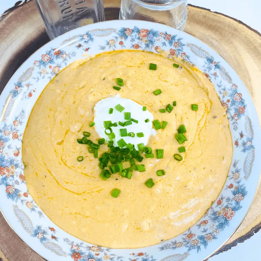 Warm Gouda, tahini, and cream cheese dip served in a floral-patterned bowl, topped with a dollop of sour cream, chopped green onions, and a drizzle of olive oil.