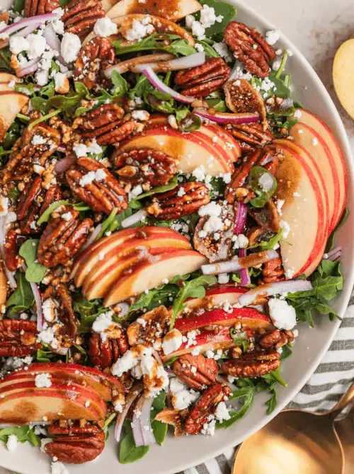 Fresh fall salad with sliced apples, candied pecans, feta cheese, red onions, and arugula drizzled in balsamic vinaigrette—a crisp, colorful option for easy fall recipes and delicious things to make with apples.
