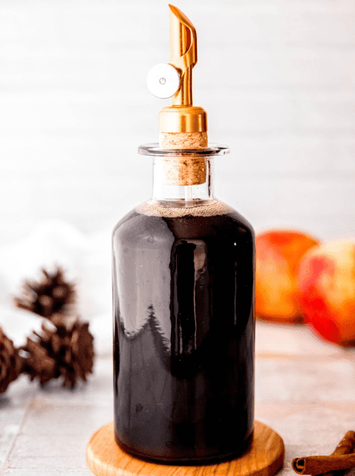 Glass bottle of homemade apple brown sugar syrup with a gold pour spout – a cozy and versatile simple fall treat and one of the easiest things to make with apples for drinks and desserts.