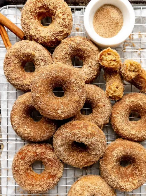 Golden baked apple cider donuts coated in cinnamon sugar, displayed on a wire rack—perfect inspiration for what to make with apples and fall bread recipes.