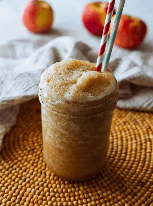 Frozen apple cider slushie in a mason jar with red and blue striped straws—icy, refreshing, and one of the most fun things to make with apples for kid-friendly fall recipes or seasonal drinks.