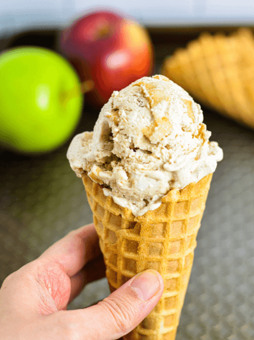 Hand holding a waffle cone filled with no-churn apple cinnamon ice cream – a fun and unexpected simple fall treat and one of the most creative things to make with apples.