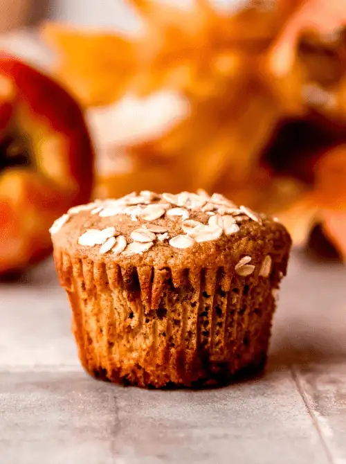 Apple Cinnamon muffin topped with oats, set against a fall backdrop—an easy, wholesome idea for what to make with apples and a nourishing fall bread recipe.