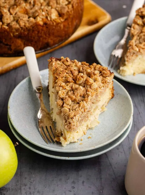 Slice of apple crumble coffee cake with oat streusel topping on a blue plate—one of the best fall desserts and a cozy, crowd-pleasing thing to make with apples for brunch or dessert.