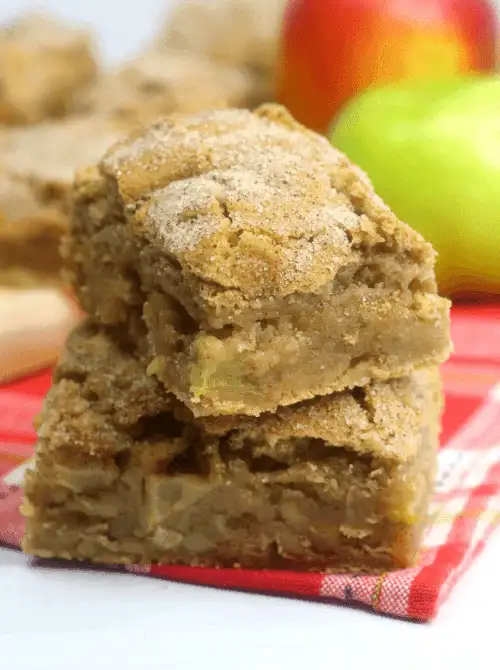 Stack of apple blondies with cinnamon sugar topping, surrounded by fresh apples—an easy, handheld fall dessert and one of the tastiest things to make with apples for snacking or sharing.