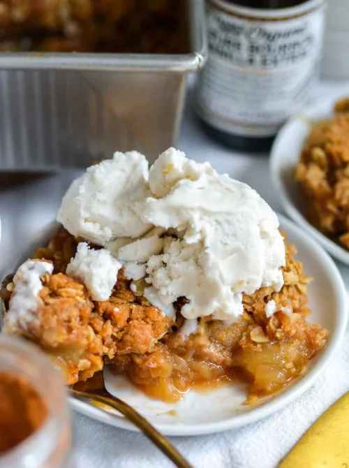 Warm vegan apple crumble with oat topping and dairy-free ice cream on a white plate—cozy and crowd-pleasing, one of the best fall desserts and tastiest things to make with apples.