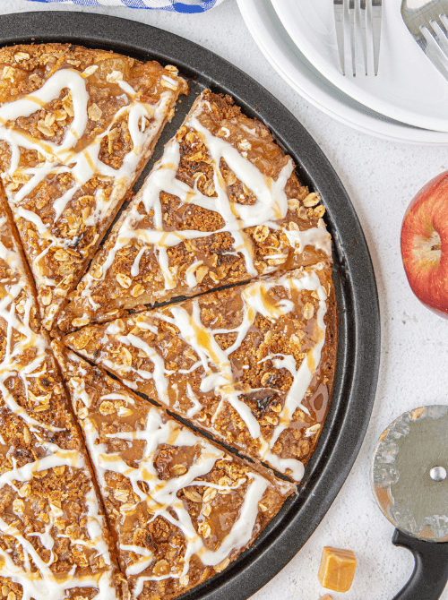 Caramel apple dessert pizza topped with oats and vanilla icing drizzle, sliced and ready to serve – a fun and simple fall treat and one of the best things to make with apples.